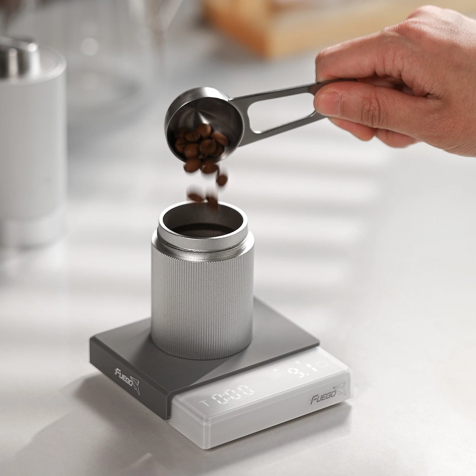 Person measuring coffee beans into a container on a digital scale with a blurred kitchen background.