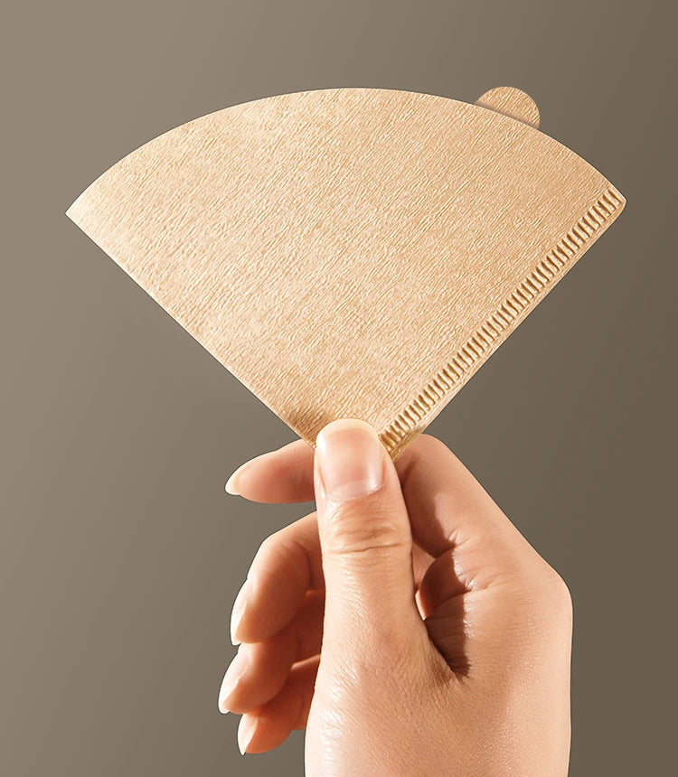 Hand holding a beige coffee filter against a plain background