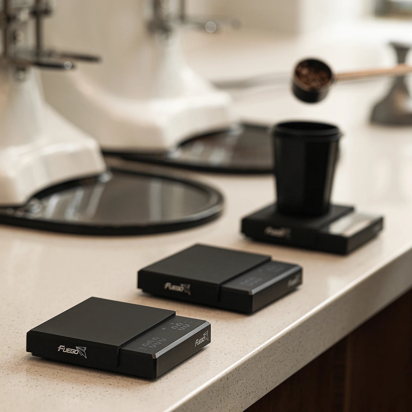 Two black electronic devices on a kitchen counter with a blurred coffee-making appliance in the background.