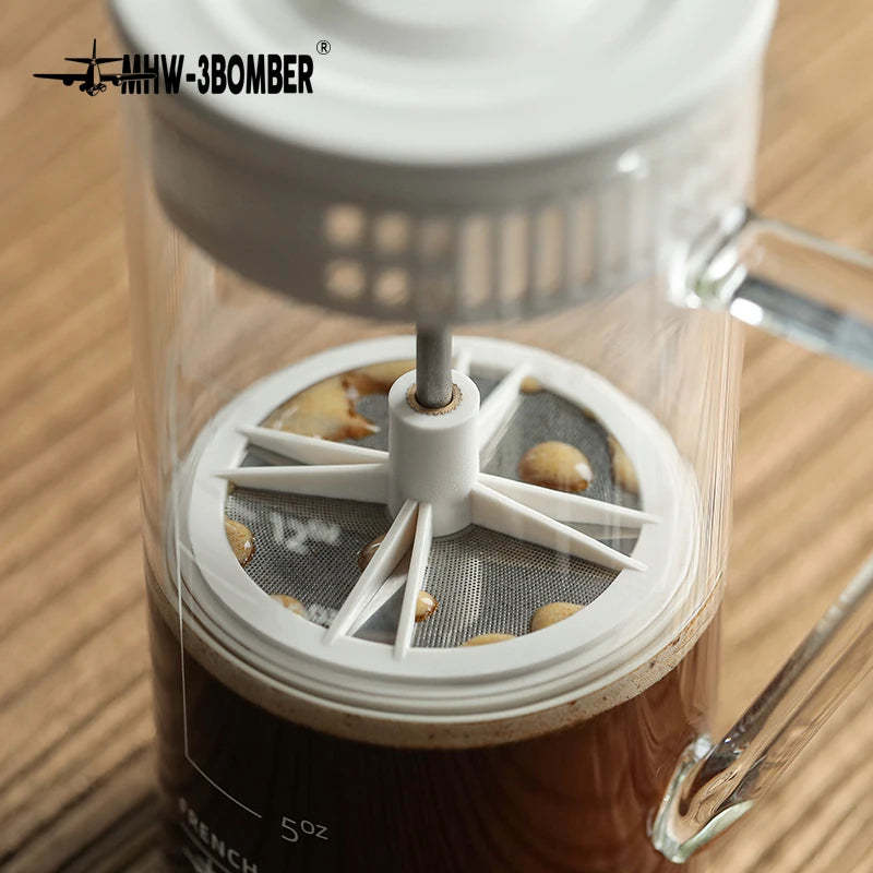 French press with coffee beans and a visible brand logo on a wooden surface
