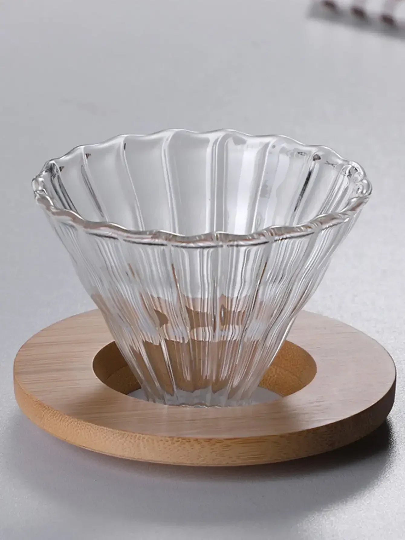 Clear glass coffee filter on a wooden base against a light gray background