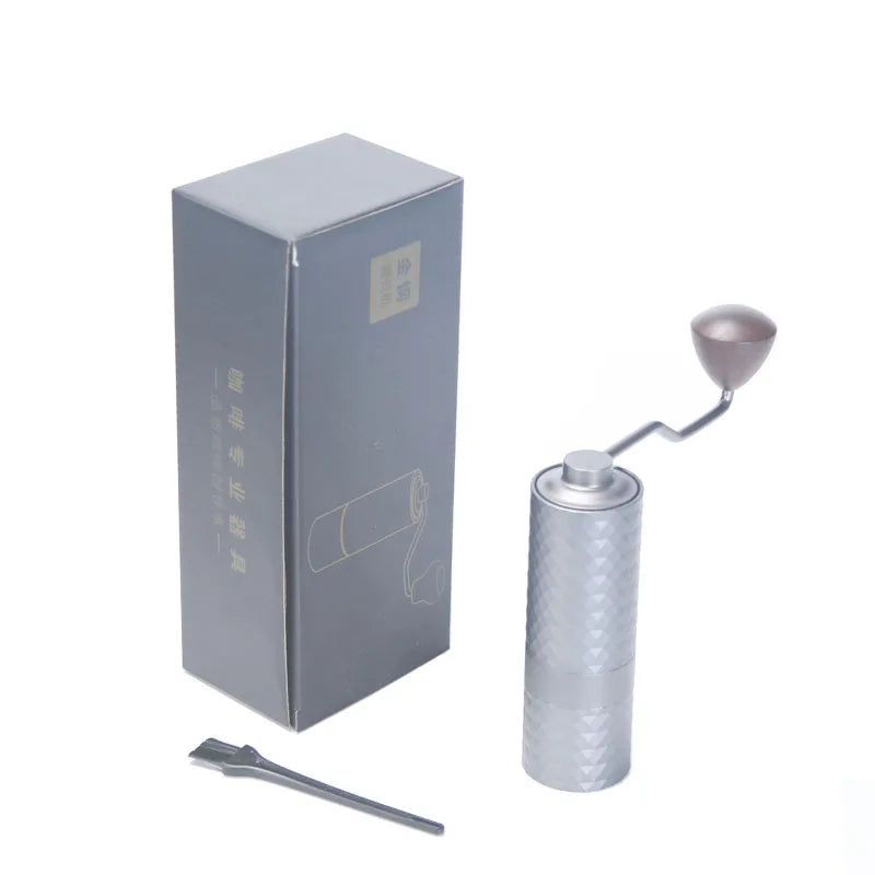Silver manual coffee grinder with packaging and tool on a white background