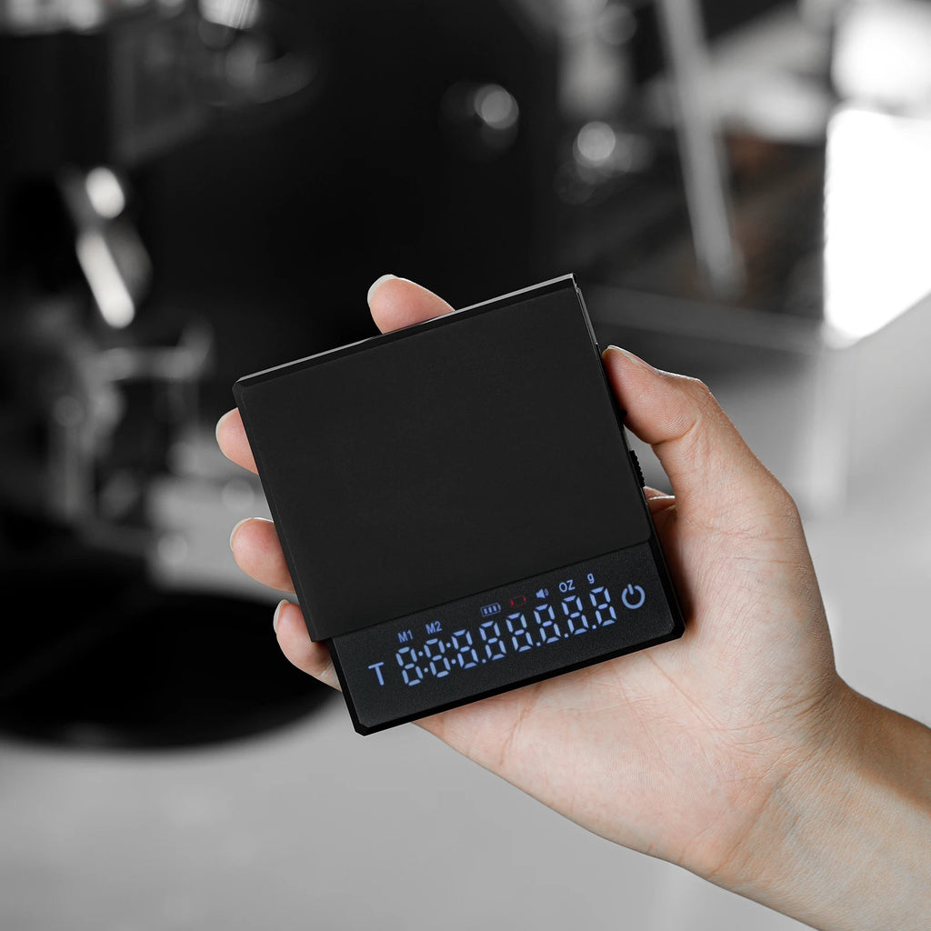 Hand holding a small electronic device with a digital display in an indoor setting