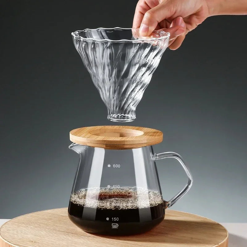 Glass coffee maker with wooden lid and hand holding a glass filter on a dark background