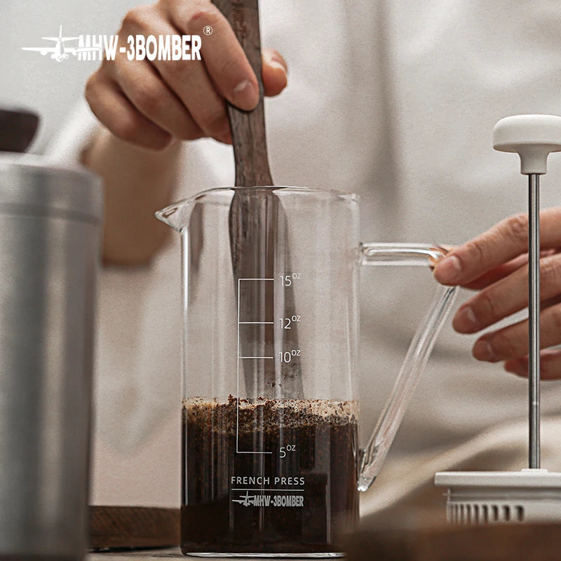 Person preparing coffee using a French press with a clear measuring cup filled with grounds.