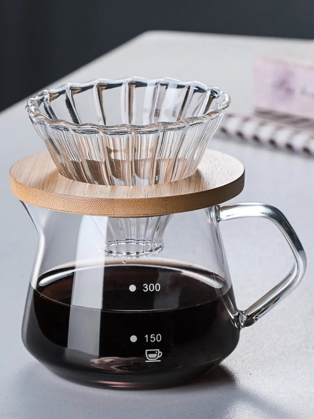 Glass coffee maker with wooden lid and glass carafe on a light surface