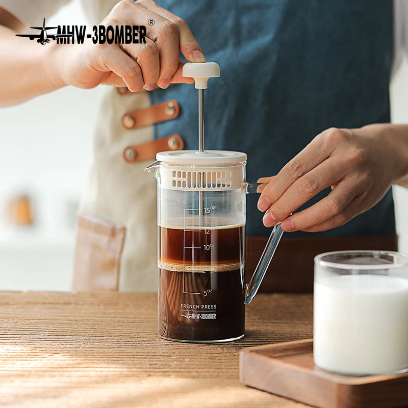 Person using a French press to make coffee on a wooden table with a blurred background.